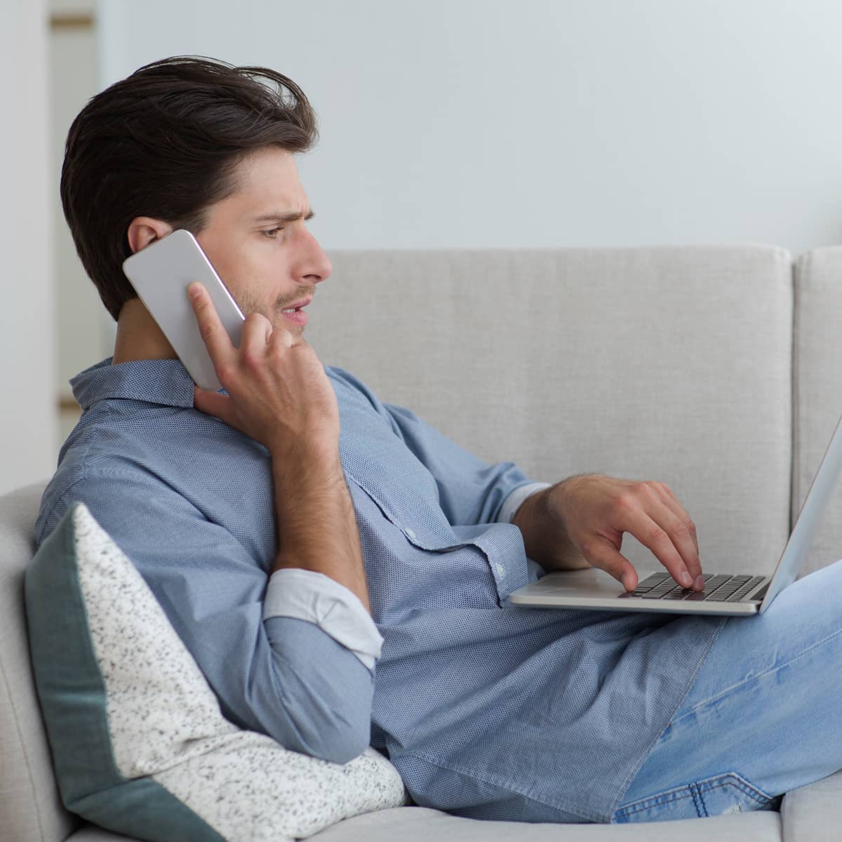 A man laying on a couch with a laptop and phone